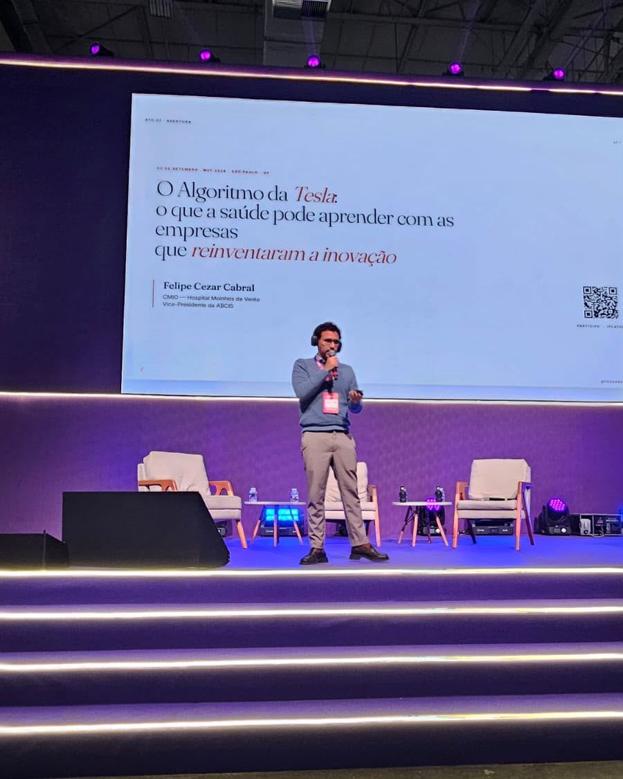 Felipe Cezar Cabral no palco do MV Experience Forum 2026, com o slide de abertura de O Algoritmo da Tesla ao fundo